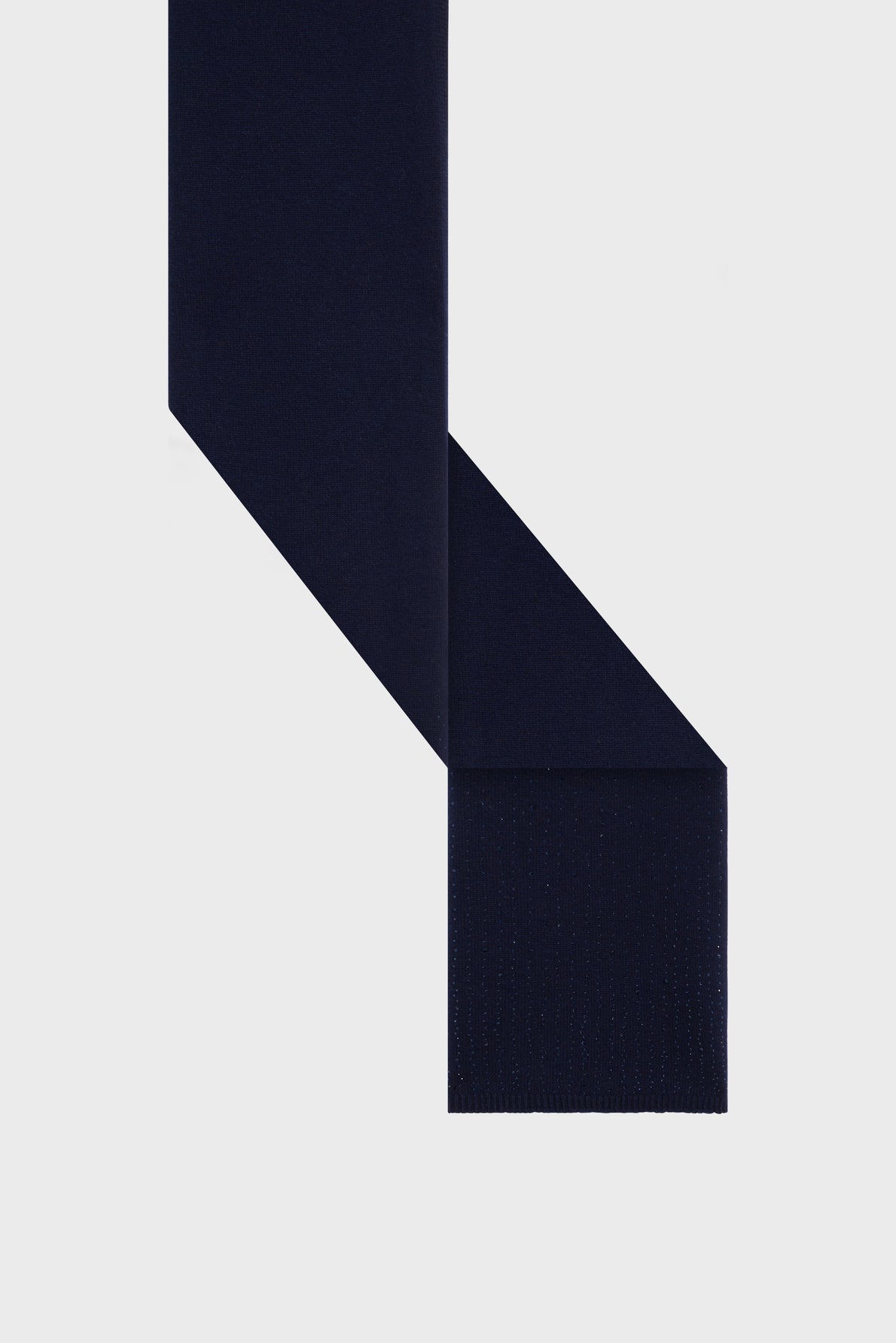 A navy blue tie with a straight edge, reminiscent of bleu marine, is arranged on a light gray background, forming an abstract geometric shape.