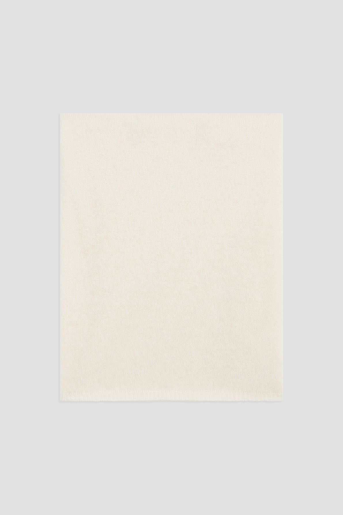 A plain, square, off-white cloth napkin is laid flat on a light gray background, evoking the soft elegance of an écharpe cachemire.