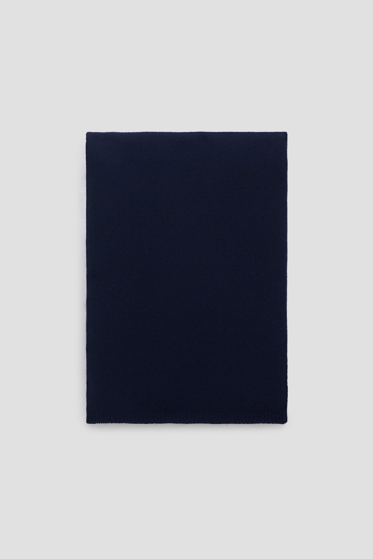 A neatly folded, solid bleu marine cachemire rectangular écharpe is displayed on a plain light gray background.