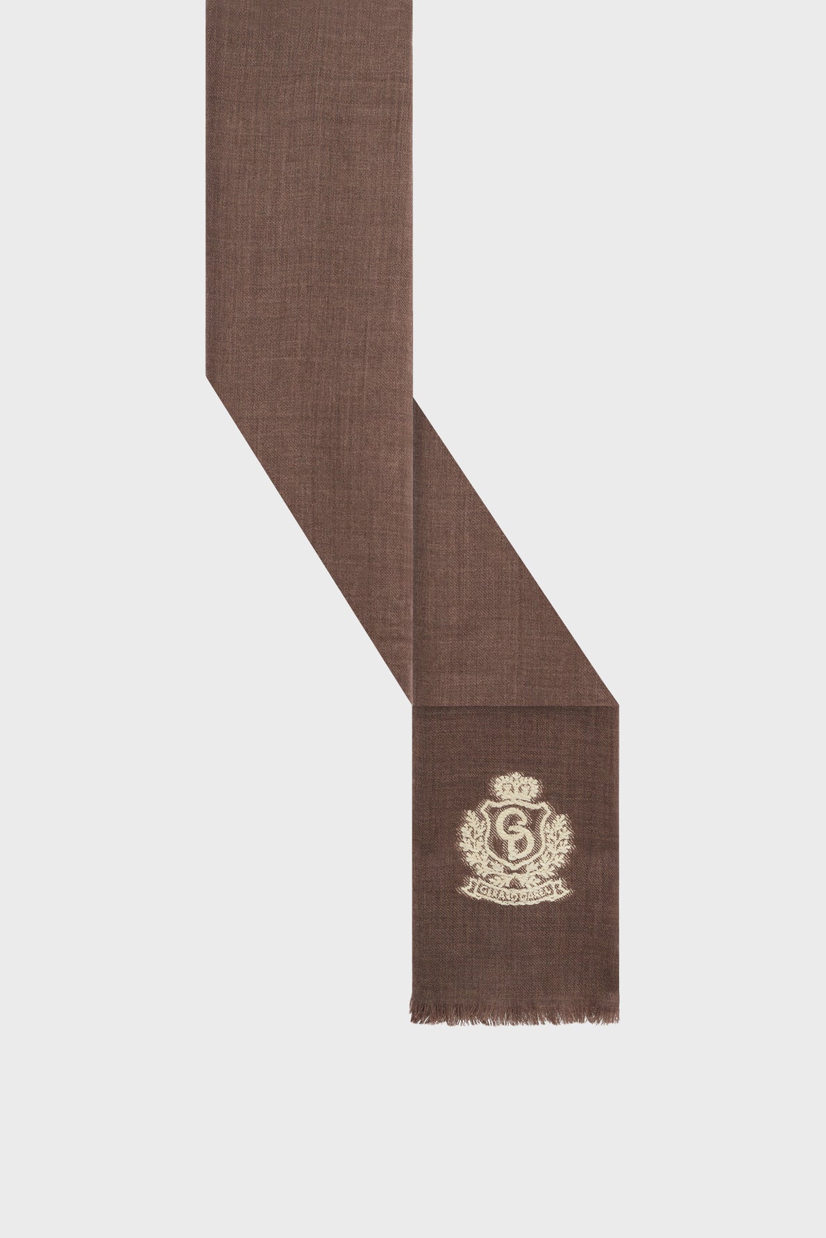 A brown scarf with a fringed edge, featuring a white embroidered crest and monogram near one end, displayed against a plain white background—this écharpe marron exudes a timeless preppy elegance.