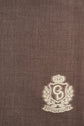 Brown textured fabric with a light-colored embroidered crest in the bottom right corner, featuring a wreath, crown, and the letters CH and AAREN—a classic touch to this élégante écharpe marron. Perfect for those seeking an écharpe preppy style with timeless sophistication.
