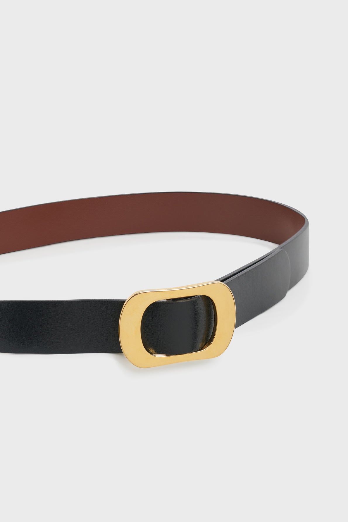 A black ceinture cuir with a gold oval buckle is displayed on a white background. The inner side of the belt is brown, making it a stylish ceinture réversible for versatile wear.