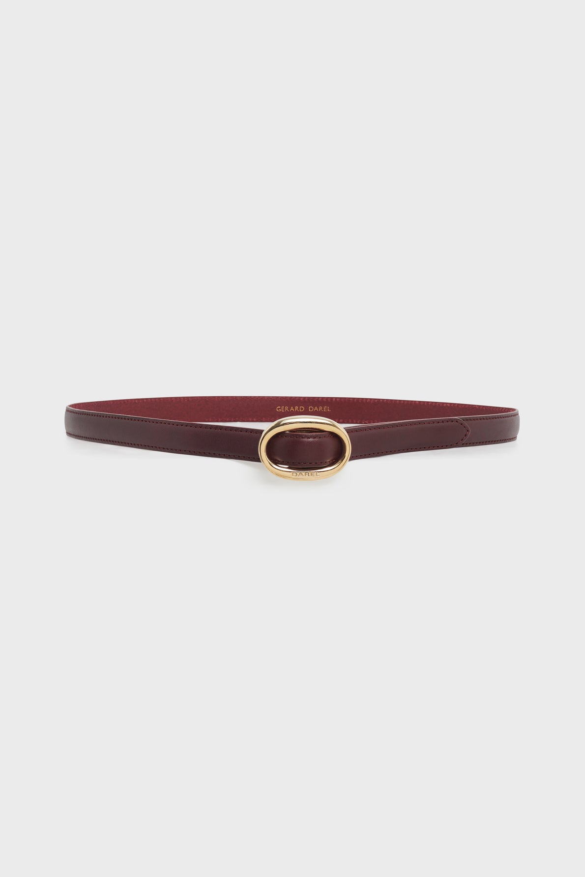 A slim, dark red leather ceinture Sofia with a gold oval buckle is displayed against a plain white background. This ceinture réglable adds an elegant touch to any outfit, making it the perfect ceinture femme for sophisticated styling.