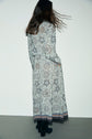 A woman with long brown hair stands with her back to the camera, wearing a jupe midi à motif floral and black boots, her hair slightly swaying as if she just turned. The skirt features a taille élastiquée for added comfort and effortless style.
