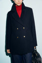 Person wearing a chic manteau mi-long, reminiscent of a black double-breasted coat with gold buttons over a red turtleneck, holding a black handbag. The luxurious laine vierge elevates the look, while only the lower half of the face is visible against a light background.