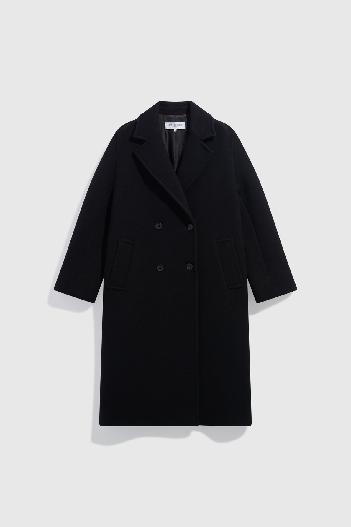 A chic à la française, long, black double-breasted overcoat crafted from luxurious drap de laine, featuring wide lapels and two front flap pockets, displayed against a plain light gray background.