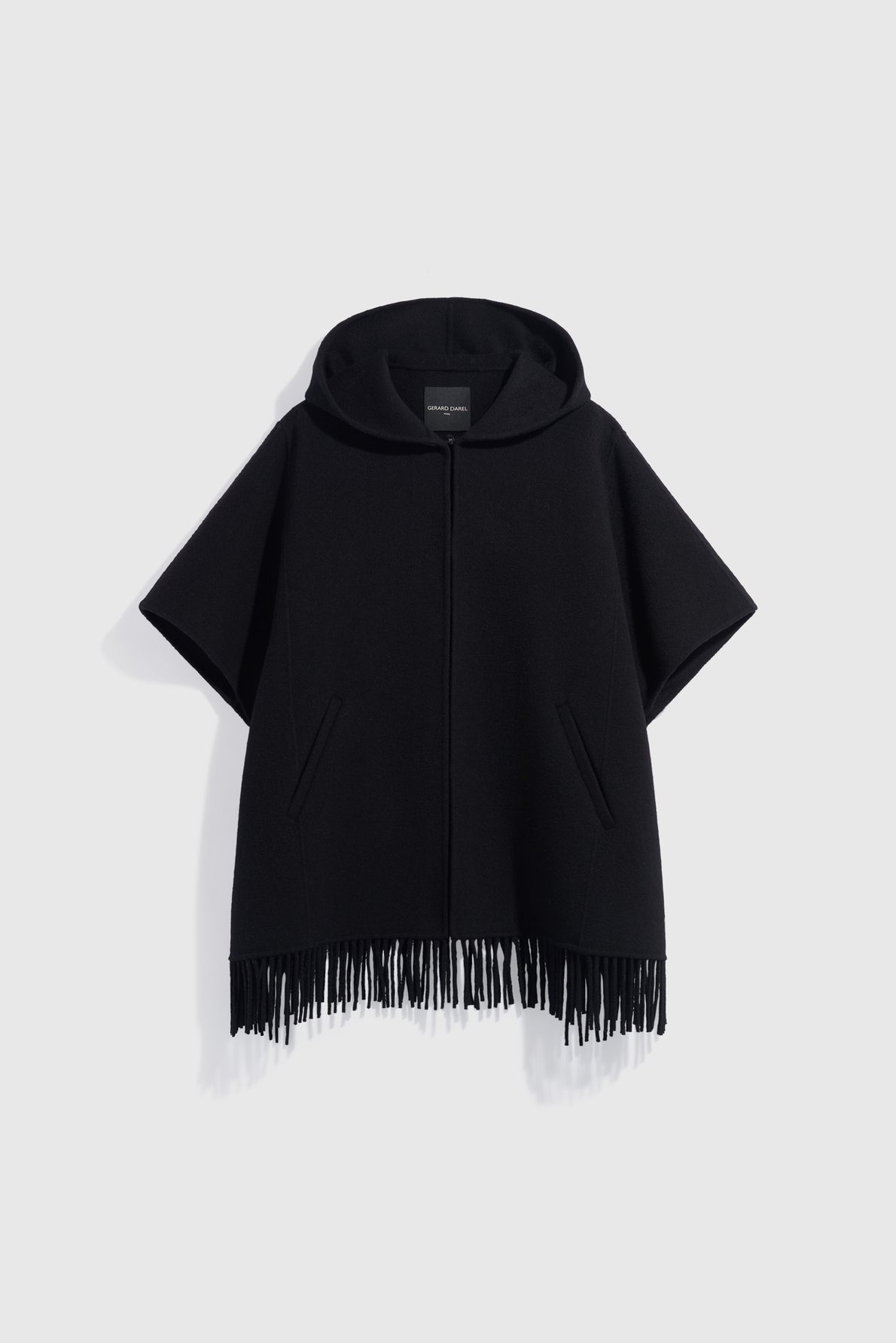A black, short-sleeved cape à capuche with a zipper front, two side pockets, and fringe detailing along the bottom hem, displayed against a plain light background.