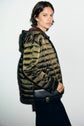 A person wearing a shiny green doudoune légère and carrying a black crossbody bag stands against a plain light background, looking at the camera.