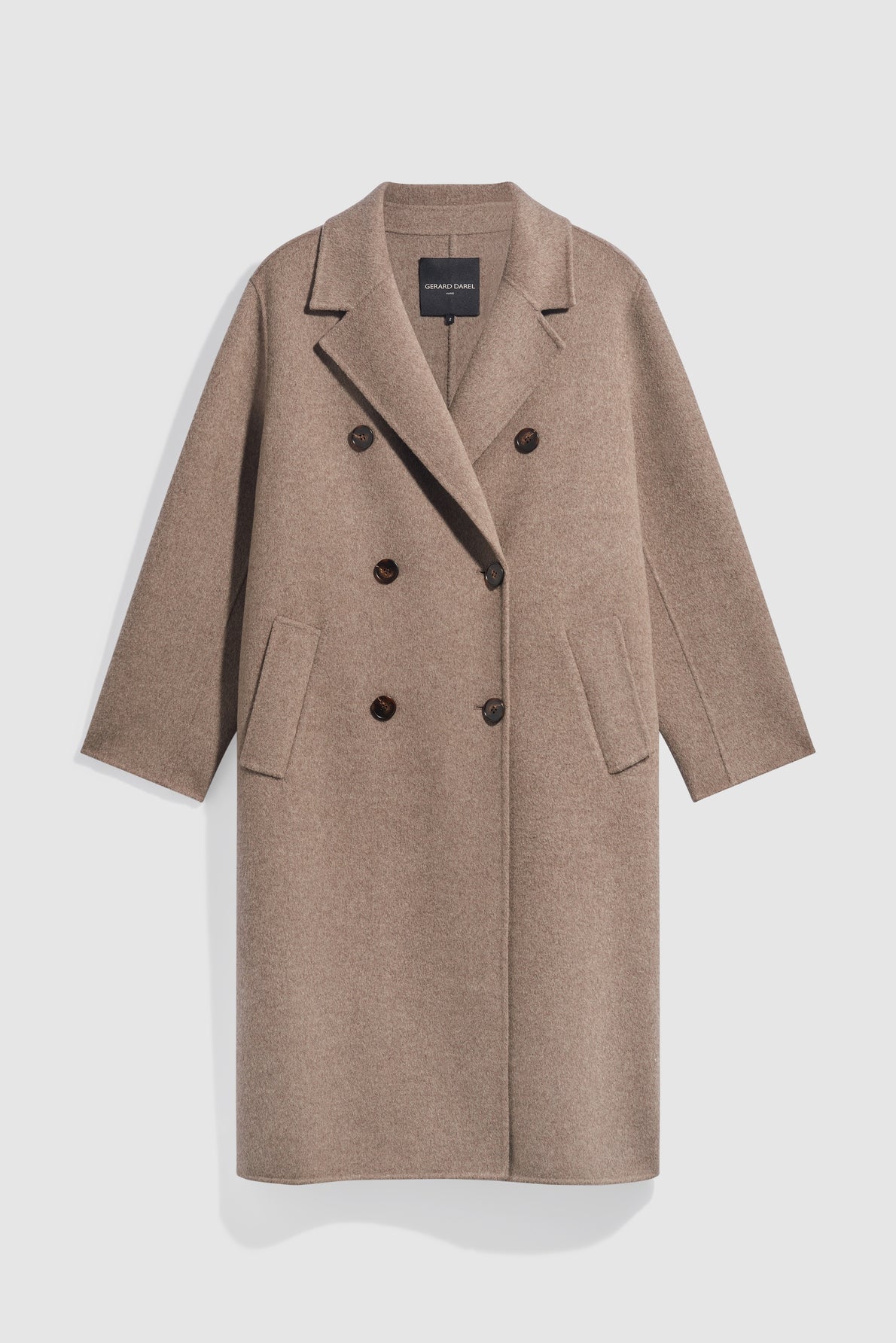 A long, light brown manteau double boutonnage in wool with black buttons, two front pockets, and a notched lapel, displayed against a plain white background.