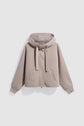 Light beige zip-up hoodie with a hood, long sleeves, ribbed cuffs, two front pockets, and wide drawstrings, displayed on a light background—this élégante veste à capuche femme offers both comfort and style for everyday wear.