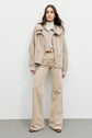 Woman standing against a plain background, wearing a beige doudoune and high-waisted beige pants paired with brown shoes. She has long, straight hair and a neutral facial expression, giving her outfit a refined yet effortlessly chic look.