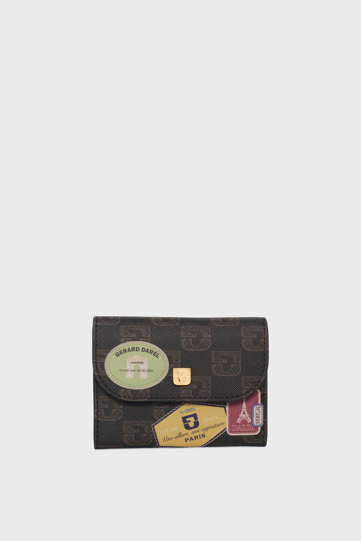 A small, rectangular, patterned wallet—this portefeuille super plat features a gold clasp and is decorated with vintage-style travel stickers in green, yellow, and red tones, all set against a plain white background.