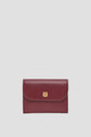 A small, burgundy leather wallet with a gold clasp is centered on a plain light gray background, perfectly embodying the elegance of a portefeuille super plat and the practicality of a petit portefeuille cuir.