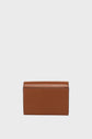 A small, rectangular petit portefeuille cuir is standing upright against a plain, light gray background.