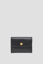 A black leather wallet with a curved flap and a small gold square clasp, this portefeuille XS femme is designed to be a petit portefeuille cuir that’s both chic and practical, set against a plain light gray background.