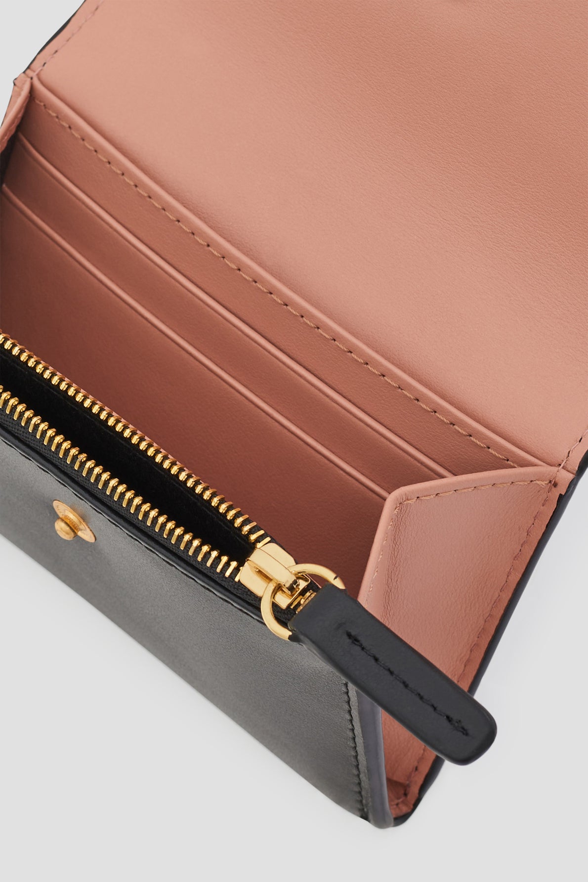 Close-up of an open portefeuille XS femme with a pink interior featuring card slots, a zippered coin pocket with a gold zipper, and black exterior trim. This petit portefeuille cuir combines elegance and practicality in a compact design.