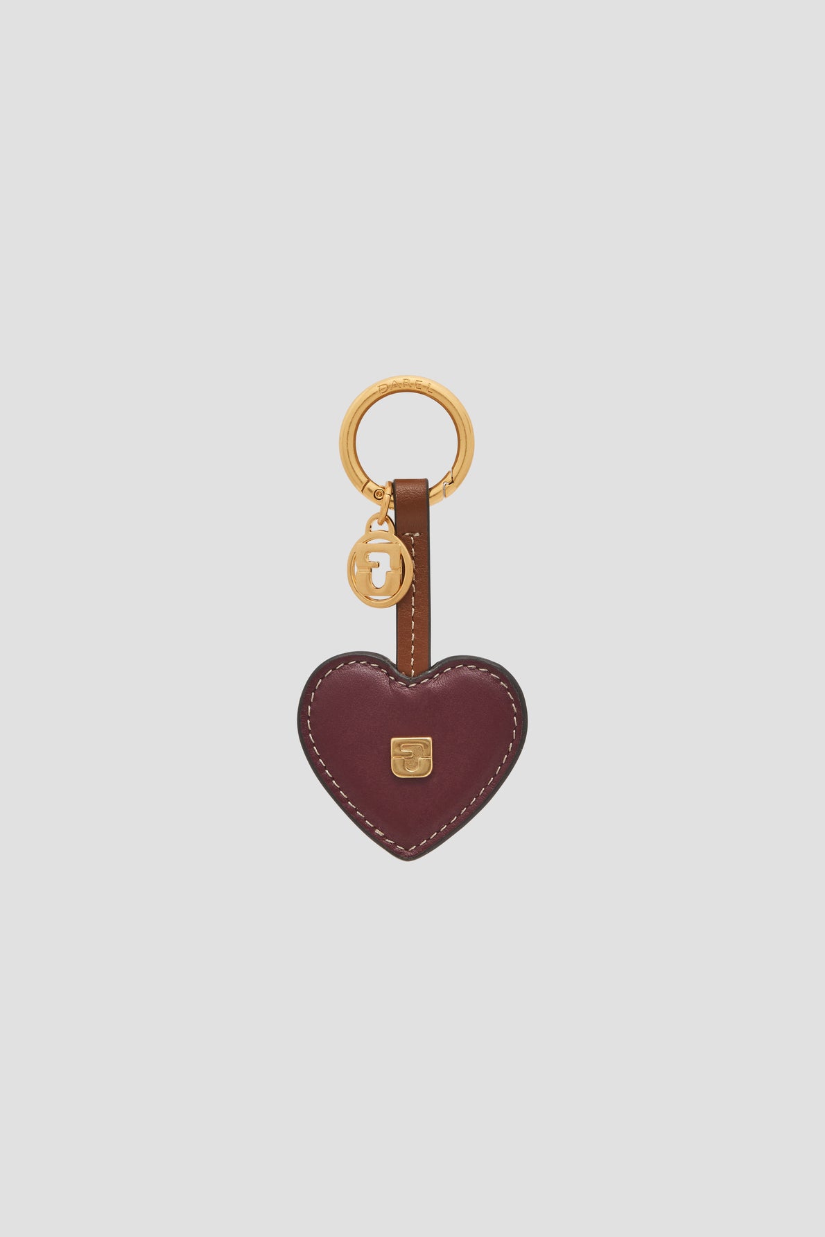 A burgundy leather heart-shaped keychain—porte-clé cœur cuir—with white stitching, a gold keyring, and a small gold charm embossed with the letter J.