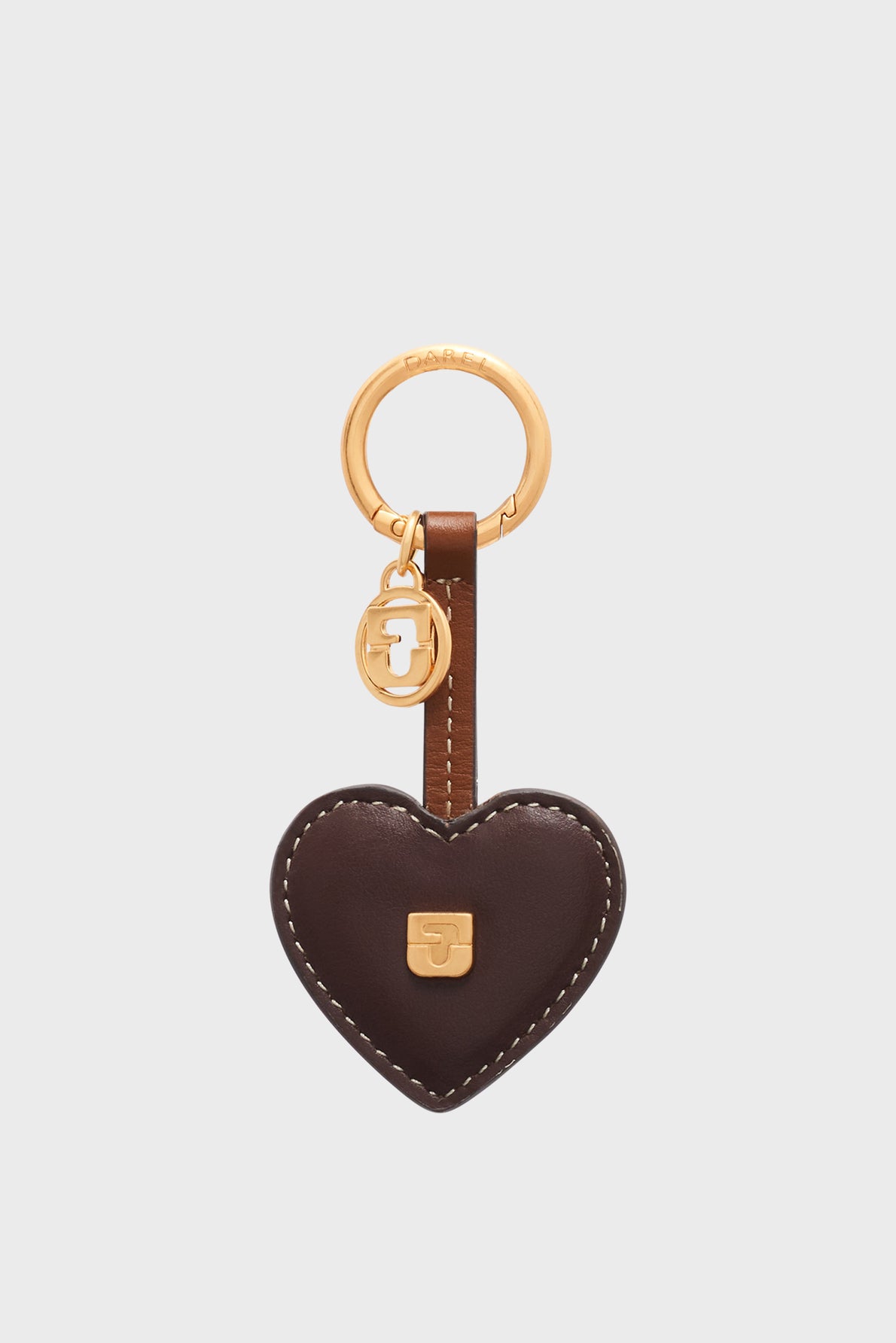 Brown leather heart-shaped keychain with visible stitching, featuring a gold-tone keyring and small round charm. This elegant porte-clé cœur cuir also boasts a small gold emblem on the front, reminiscent of a chic accessoire sac femme. The keychain is displayed on a plain light background.