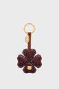 A porte-clé trèfle featuring a gold ring and a dark red, four-leaf clover charm crafted from heart-shaped cuir de vachette petals, adorned with gold logo accents and detailed white stitching along the edges. This keychain is both a stylish accessory and a porte-bonheur to carry with you.
