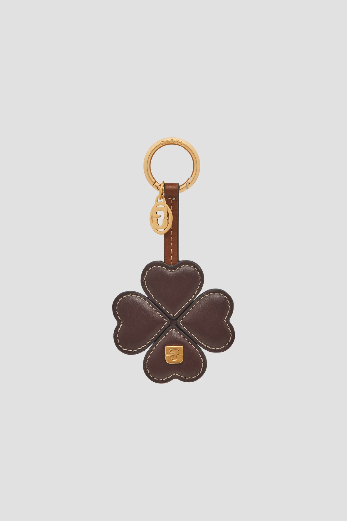A brown leather keychain shaped like a four-leaf clover with white stitching, a gold ring, and a small gold charm attached—a stylish porte-clé trèfle that brings good luck wherever you go. This porte-bonheur cuir accessory is both elegant and unique, perfect for adding a touch of charm en cuir to your everyday essentials.