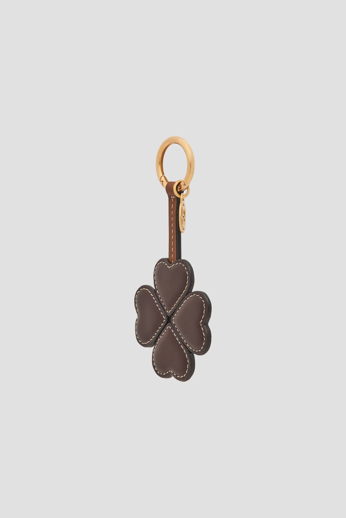 A brown leather keychain shaped like a four-leaf clover with white stitching and a gold key ring, this porte-clé trèfle is a delightful porte-bonheur cuir to bring luck and style wherever you go.