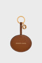 A round brown leather keychain with GERARD DAREL in gold letters, a gold ring, and a small gold charm with a raised G embodies the élégance parisienne and timeless allure charm that define the Gerard Darel brand.