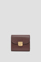 A small brown Gerard Darel portefeuille cuir with a gold clasp is centered on a plain light gray background.