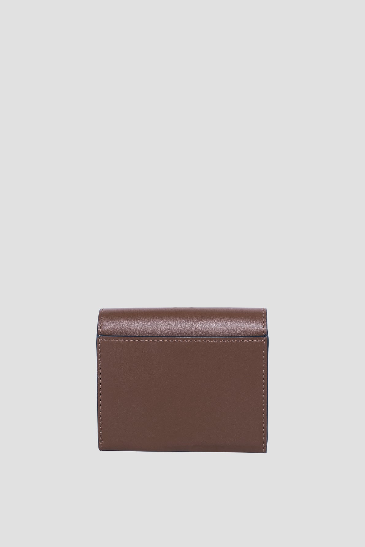 A small, rectangular brown leather wallet from Gerard Darel is displayed standing upright against a plain light gray background. This portefeuille cuir compact is closed, showcasing its smooth exterior with visible stitching along the edges.