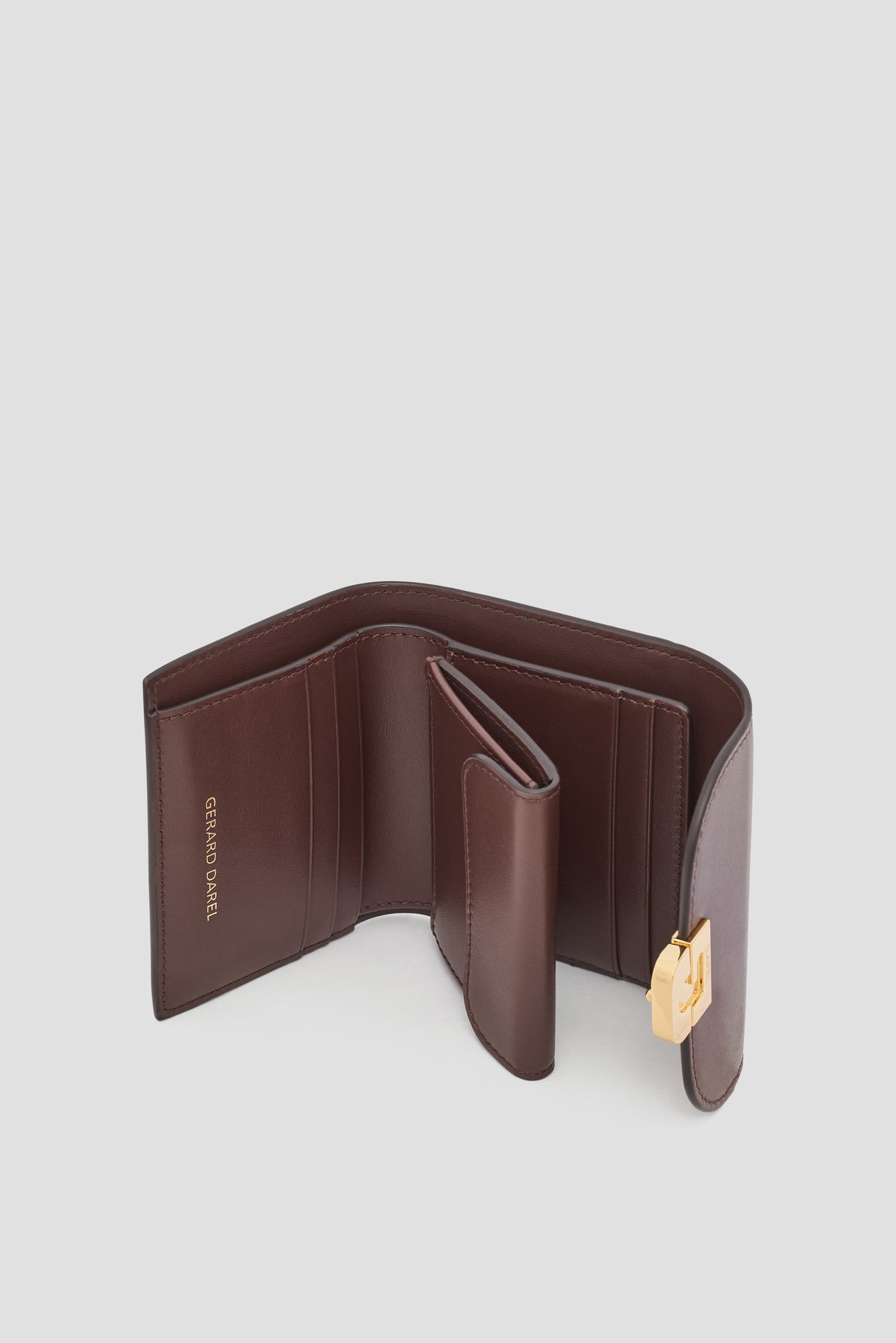 A brown portefeuille cuir wallet with multiple compartments, a gold clasp, and GRAND BONHEUR embossed on the inside pocket, displayed open on a plain light background. This elegant portefeuille compact reflects the timeless style of Gerard Darel.