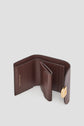 A brown portefeuille cuir wallet with multiple compartments, a gold clasp, and GRAND BONHEUR embossed on the inside pocket, displayed open on a plain light background. This elegant portefeuille compact reflects the timeless style of Gerard Darel.