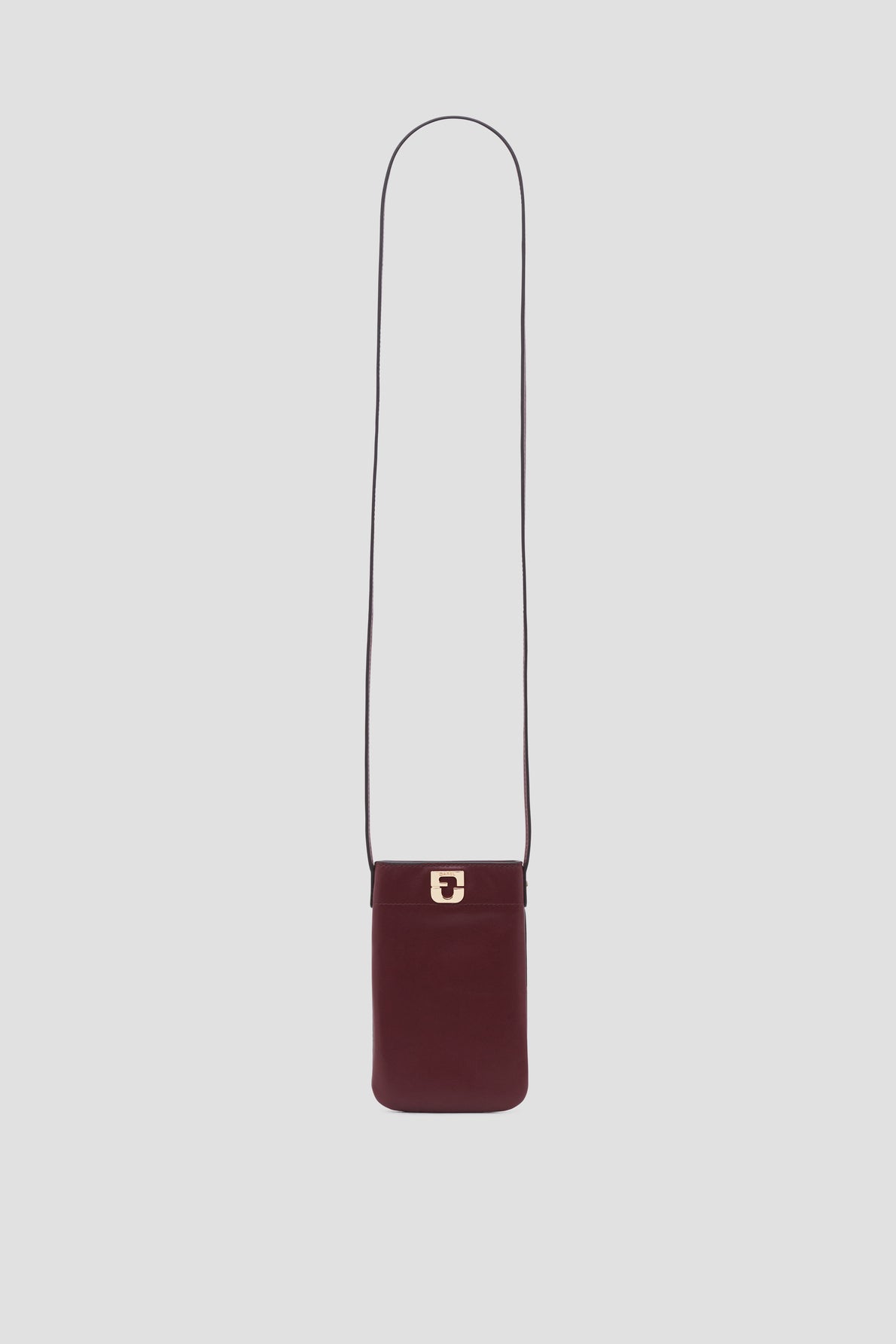 A small, rectangular burgundy shoulder bag crafted from porte-téléphone cuir with a long thin strap and a gold-tone clasp on the front, this accessoire tendance is displayed against a plain light gray background.