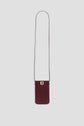 A small, rectangular burgundy shoulder bag crafted from porte-téléphone cuir with a long thin strap and a gold-tone clasp on the front, this accessoire tendance is displayed against a plain light gray background.