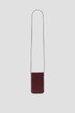 A small, rectangular burgundy leather crossbody bag with a long, thin strap—perfect as a porte-téléphone cuir and displayed against a plain light gray background—makes for an accessoire tendance to elevate any outfit.
