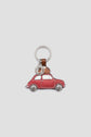 A charming porte-clés Gérard Darel featuring a small red car with a bear driving, attached to a silver key ring and brown leather strap on a plain light background.