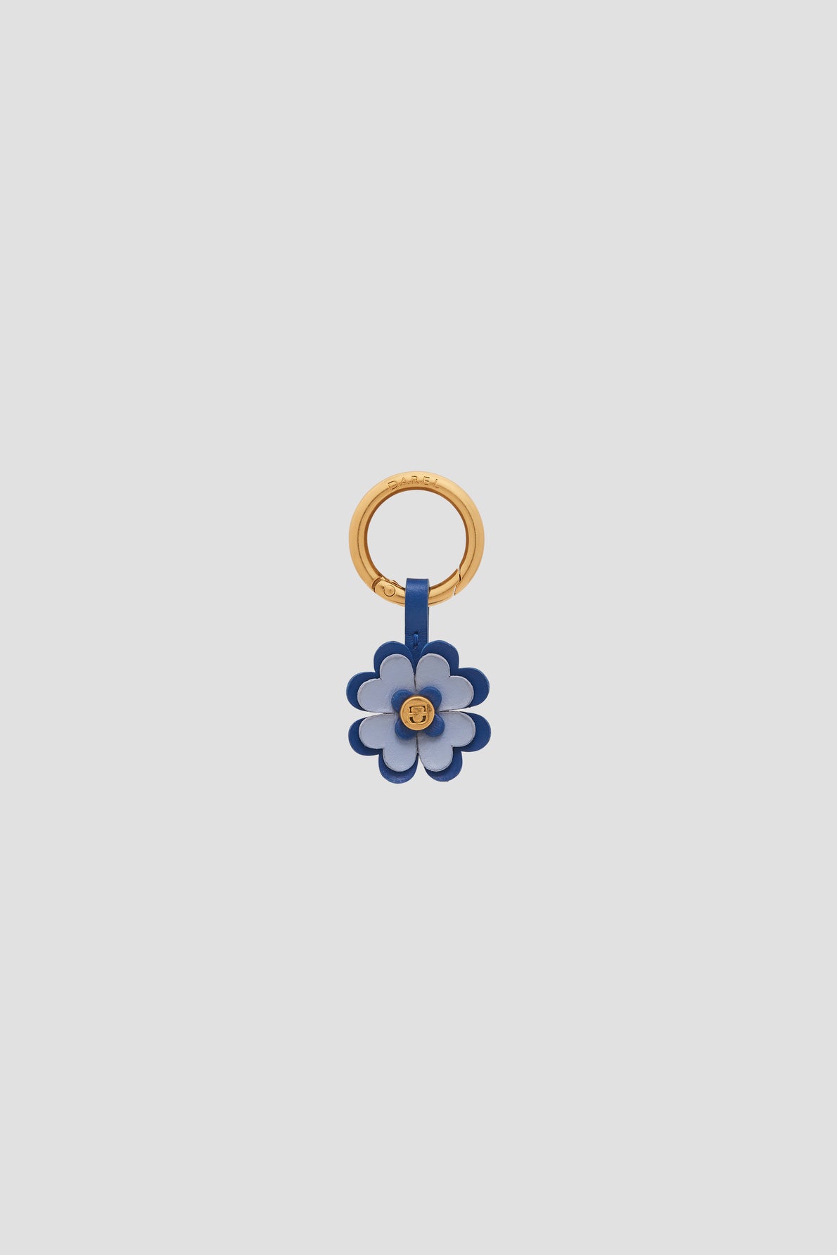 A gold keyring with a blue and white charm en cuir flower attached, featuring a gold stud at the center—an elegant porte-bonheur and perfect accessoires de sac—displayed on a plain light gray background.