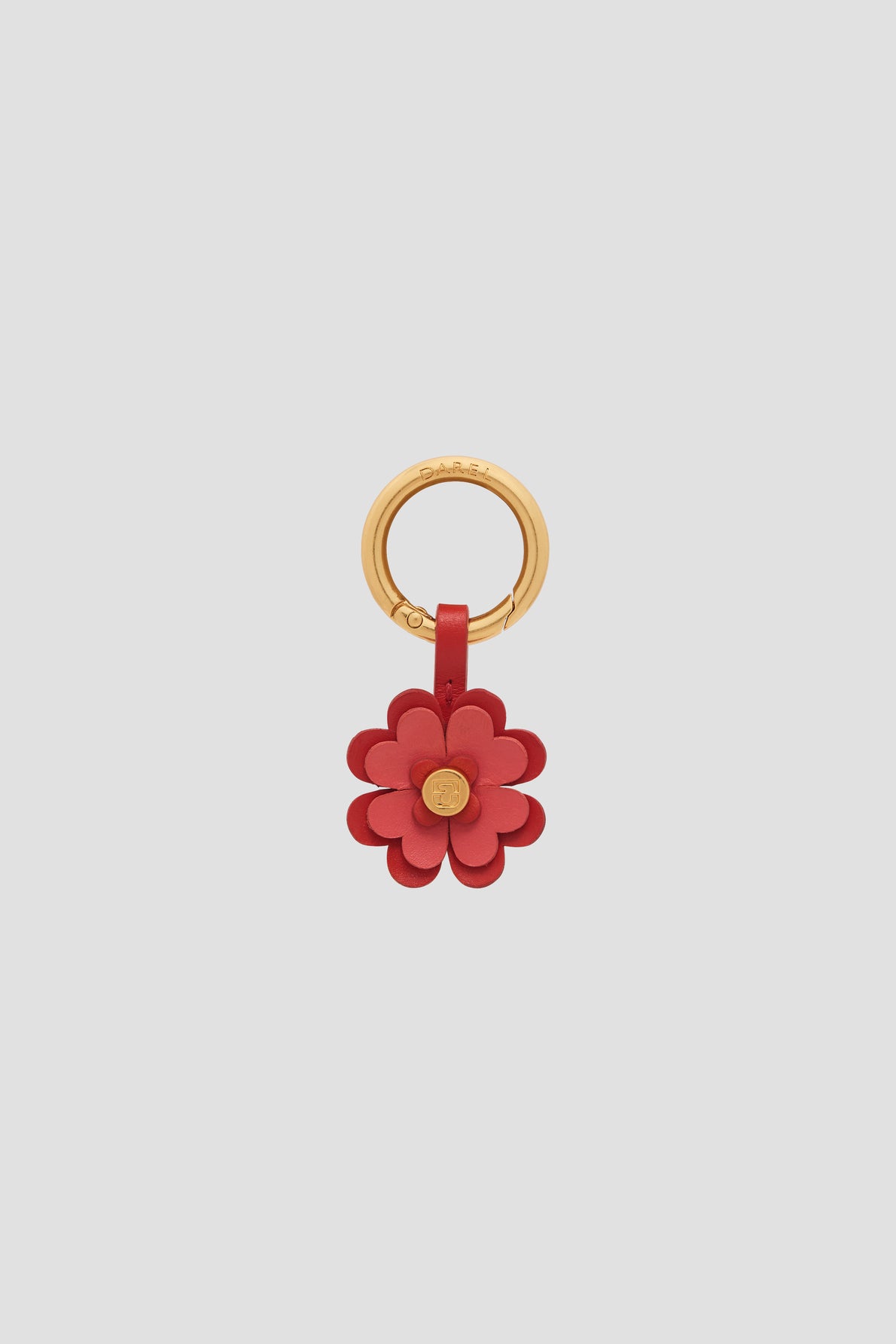 A gold keyring with a red charm en cuir flower, featuring layered petals and a small gold center—a bijou luxe accessory that doubles as a porte-bonheur.