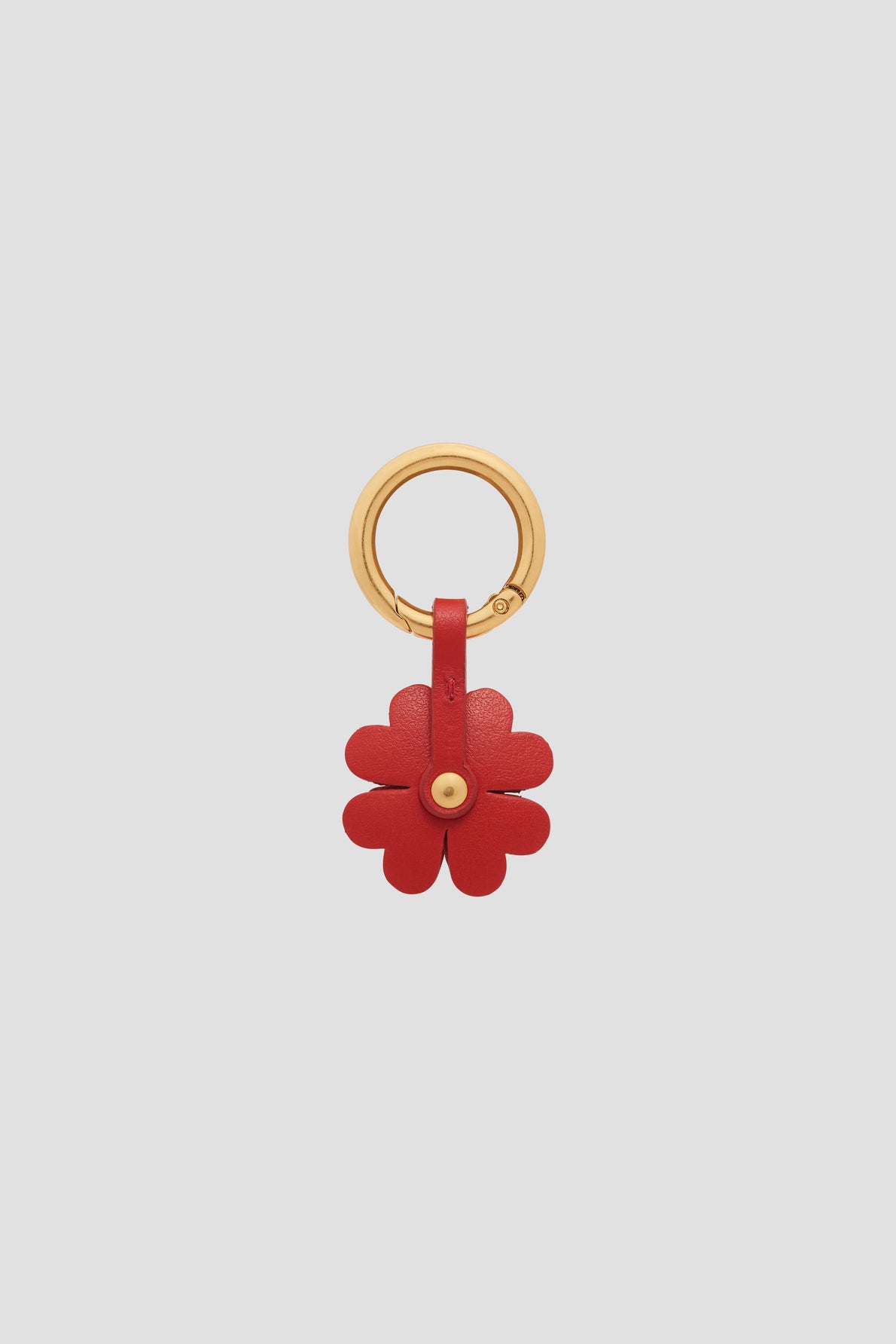 A gold keyring with a red leather flower charm en cuir attached by a small strap. The flower has rounded petals and is fastened at the center with a gold-colored stud, creating an elegant bijou luxe feel. The background is plain light gray.