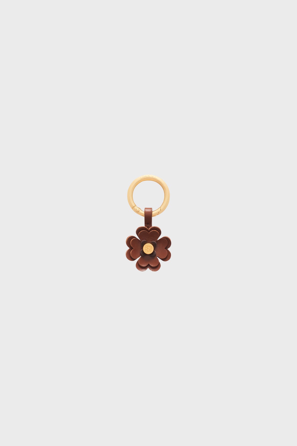 A gold keyring with a brown charm en cuir flower featuring layered petals and a small gold center, displayed on a plain light background—an elegant bijou clé that doubles as a porte-bonheur for everyday carry.
