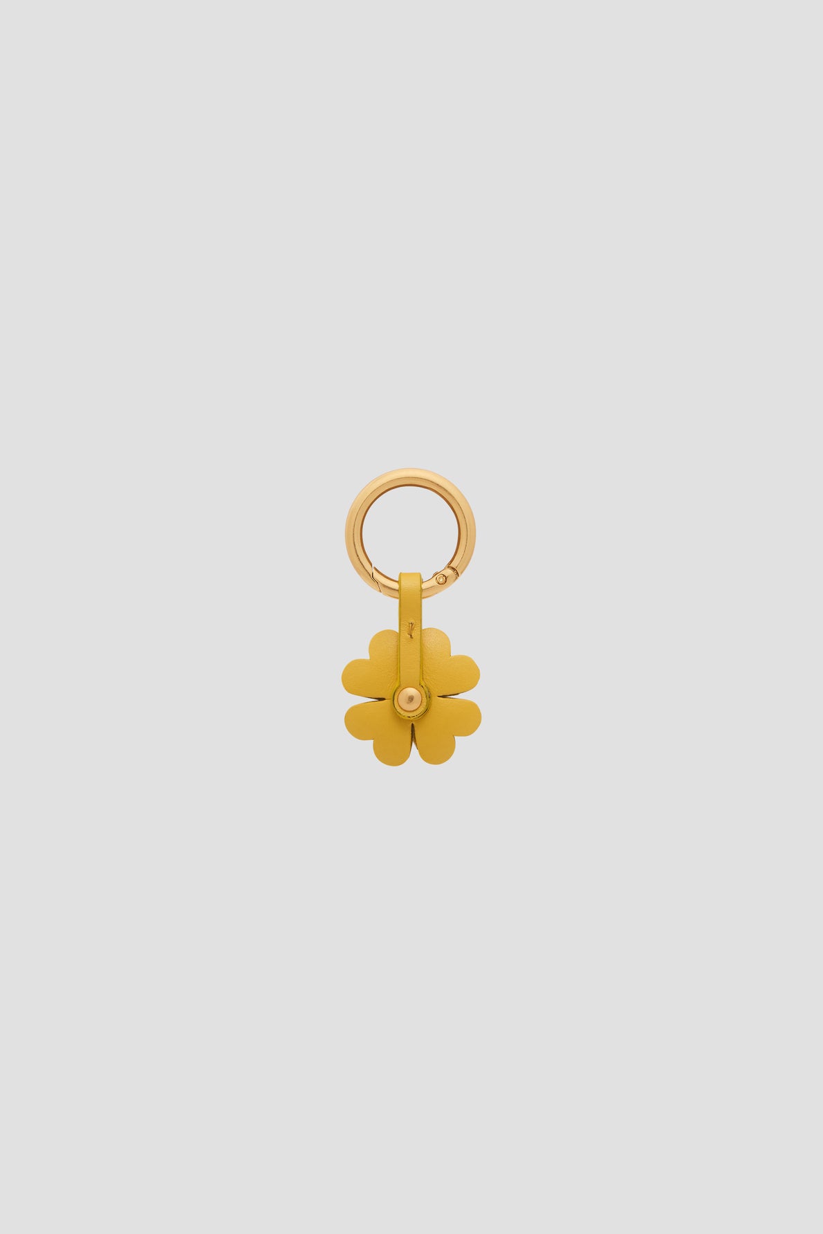 Gold keychain with a circular clasp and a hanging four-leaf clover charm, this porte-bonheur accessoire clé is photographed on a plain light gray background.