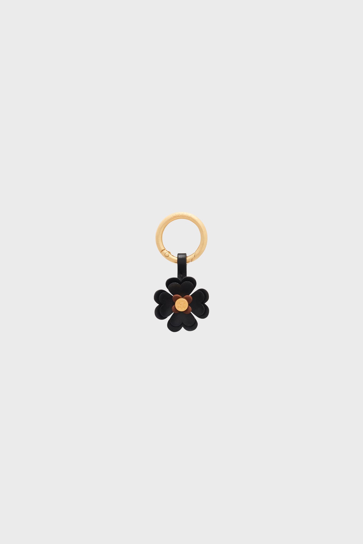 Gold keyring with a black flower-shaped charm en cuir and a gold center, displayed on a plain light gray background—an accessoire clé that adds a touch of bijou porte-bonheur to your everyday essentials.