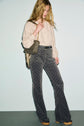 A woman with long blonde hair wears a beige blouse, a pantalon taille haute with a striking pattern, platform shoes, and carries a quilted shoulder bag while looking down.