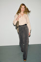 A woman with long blonde hair walks forward wearing a beige blouse, patterned gray pantalon taille haute, platform shoes, and carrying a gold chain-strap bag. She poses confidently against a plain background.