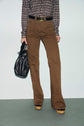 Person wearing a patterned long-sleeve shirt, a pantalon cannelle taille haute flare, black belt, platform shoes, and holding a black handbag. Face not visible.