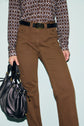 Person wearing a taille haute pantalon cannelle, a patterned brown and white shirt, and a black belt, holding a black handbag. The image shows the outfit from the shoulders down against a light background.