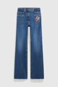 Blue, wide-leg jean flare with front pockets and a red and white embroidered patch on the right side. This pantalon long is laid flat on a plain white background.