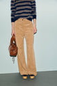Person wearing a pantalon velours côtelé beige, a blue and beige striped sweater, holding a brown leather bag, and wearing tan platform shoes, standing against a plain light background.