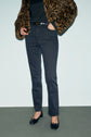 Person wearing a leopard print coat, black shirt, dark high-waisted jean slim noir with a black belt, and black ballet flats, standing against a plain background. Their face is not visible.