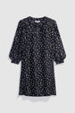 Black knee-length robe courte with a chic motif imprimé featuring white polka dots, gathered shoulders, col V, and three-quarter puff sleeves, displayed against a plain light gray background.