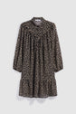 A black long-sleeve robe courte with a loose fit, featuring a tan polka dot pattern and a ruffled hem, crafted in mousseline fluide and finished with a chic col chemise, displayed against a plain light background.