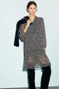 A woman wearing a black robe courte with white polka dots and black pants stands against a light background, the mousseline fluide fabric gently draping as she holds a black jacket over her shoulder. The chic col chemise detail adds an elegant touch to her look.